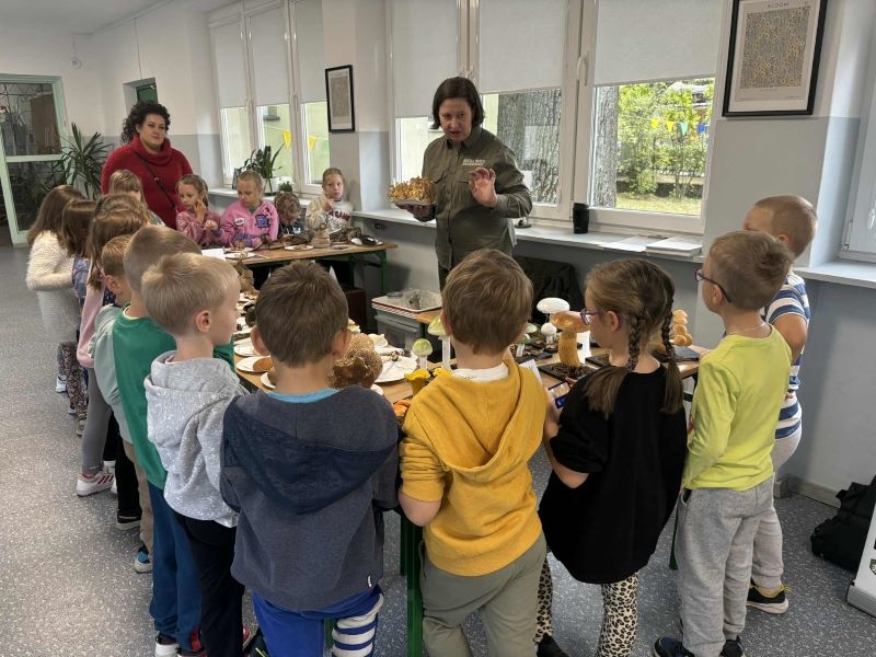 Przedstawicielka Białowieskiego Parku Narodowego pokazuje dzieciom grzyby znajdujące się na wystawie.