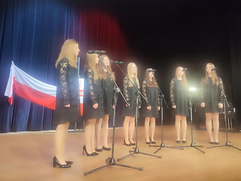 dziewczęta śpiewają na scenie w tle zawieszona dekoracja okolicznościowa