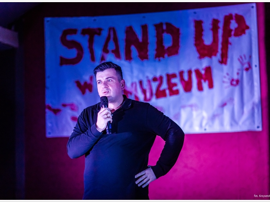 mężczyzna z mikrofonem. W tle napis STAND UP W MUZEUM