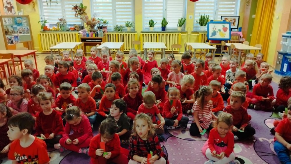 Dzieci siedzą na dywanie, w rękach trzymają karteczki w dwóch kolorach.