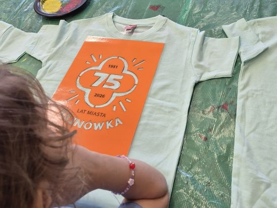 dziewczynka siedzi przy koszulce z szablonem 75 lat miasta Hajnówka