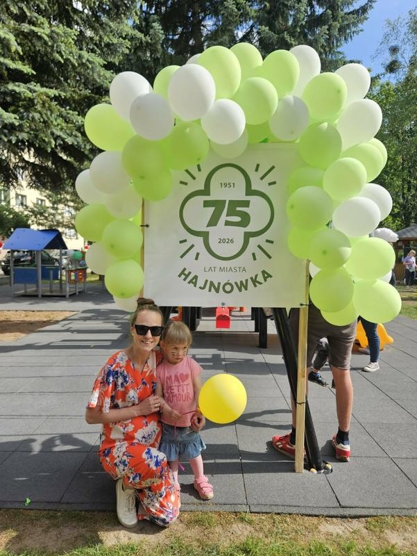 dziewczynka z kobietąpozują przy dużym logo 75 lat praw miasta Hajnówka