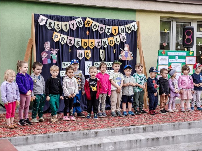 dzieci na schodach przedszkola, w tle widać napis FESTYN RODZINNY PRZEDSZKOLA NR 1