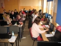 Uczestnicy szkolenia w trakcie spotkania, usadzeni są za szkolnymi ławkami, przed sobą na stolikach mają laptopy
