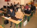 Uczestnicy szkolenia w trakcie spotkania, usadzeni są za szkolnymi ławkami, na stolikach mają laptopy