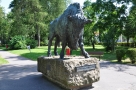 Żubrzdjęcie przedstawia pomnik żubra - wykonana z brązu figura żubra dużej wilkosci ustawiona na kamiennym cokole, z umiejscowioną tabliczką z napisem Żubr Imperator; w tle alejki parku i zieleń drzew oraz trawy