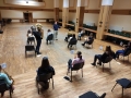 Zdjęcie robione ze sceny. Muzycy siedzą na krzesłach usadzeni tyłem do robiącego zdjęcie.