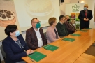Na zdjęciu pięć osób siedzi za stołem, przed nimi zielone teczki. Po prawej stronie stoi Burmistrz.