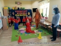Na zdjęciu widzimy dzieci w czerwonych koszulkach wspólnie z paniami przebranymi za Tygryska i Kubusia Puchatka oraz Panią Dyrektor Iwoną Raszkiewicz, które w sali tańczą, śpiewają piosenki oraz ćwiczą pokonując tor przeszkód. 