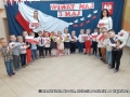 Dzieci z grupy II Kangurki ustawione w półkolu na zmianę chłopak - dziewczyna, gdzie niektóre dzieci trzymają flagę biało - czerwoną recytują wiersz "Barwy ojczyste".