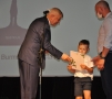 burmistrz wręcza chłopczykowi teczkę z nagrodą; obok niego stoi jego tata
