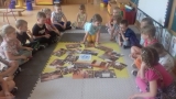dzieci siedzą na piankowym dywanie i oglądają zdjęcia przestawiające ich rówieśników, którym pomoc humanitarną niesie UNICEF. Przedszkolaki podnoszą fotografie, dyskutują na ich temat, zadają pytania.