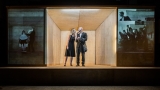 dwaj aktorzy - kobieta i mężczyzna stoją w drewnianej konstrukcji; po bokach wyświelone są czarno-białe zdjęcia
