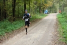 Na zdjęciu mężczyzna biegnie przez las, daleko w tle radiowóz policyjny