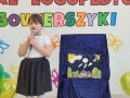 Dziewczynka recytuje wiersz, po prawej stronie zaprezentowana jest praca plastyczna.