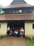 Zdjęcie grupowe uczestników wycieczki przed kremowym budynkiem z brązowym, drewnianym dachem.