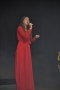 Dziewczyna w czerwonej, długiej sukni śpiewa na scenie, w ręku trzyma mikrofon.
