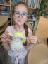 Uśmiechnięta dziewczynka w okularach prezentuje laleczkę z włóczki
