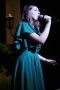 Dziewczyna w zielonej sukience śpiewa do mikrofonu, który trzyma w ręku.