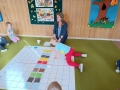 dzieci układają na dużej macie do kodowania  kolorowe kartoniki według wzoru