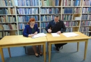 kobieta i mężczyzna usadzeni za stołem podpisują dokumenty