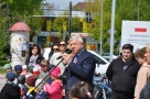 Burmistrza przemawia do mikrofonu, w tle dzieci przedszkolne i mieszkańcy miasta.