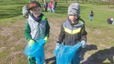 dwaj chłopcy w rekawicach trzymaja niebieskie worki na śmieci. W tle widać inne dzieci na trawiku.