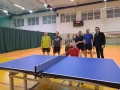 Siedmiu mężczyzn stoi na sali gimnastycznej za stołem do tenisa stołowego.