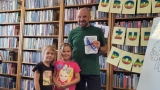 Tomasz Samojlik pozujący do zdjęcia z dwójką dzieci na tle regałów z książkami