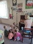 kobieta gra na pianinie, na dywanie siedzą dzieci