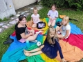 Dziewczynki siedzą na kolorowej chuście animacyjnej.