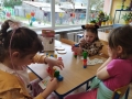  dzieci malują, bawią się, siedzą na dywanie i odnawiają temat z nauczycielem prowadzącym