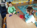  dzieci malują, bawią się, siedzą na dywanie i odnawiają temat z nauczycielem prowadzącym