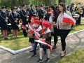 Zuchy wraz z paniami składają biało – czerwone goździki pod obeliskiem im. Konstytucji 3 Maja w miejskim parku. 