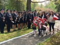 Zuchy wraz z paniami składają biało – czerwone goździki pod obeliskiem im. Konstytucji 3 Maja w miejskim parku. 