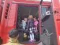 dzieci podchodzą do wozu strażackiego, robią sobie zdjęcia, z zainteresowaniem oglądają sprzęt oraz zaglądają do środka pojazdu. 