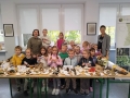 Dzieci, nauczycielki i pani leśnik stoją przy dużym stole, na którym wyeksponowane są różne gatunki grzybów.