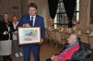Burmistrz wręcza jubilatce obraz Zbigniewa Budzyńskiego przedstawiający żubra