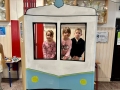  dzieci są w foto budce w kształcie lokomotywy. Wyglądają przez okienko i uśmiechają się do zdjęć.