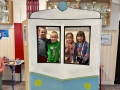  dzieci są w foto budce w kształcie lokomotywy. Wyglądają przez okienko i uśmiechają się do zdjęć.